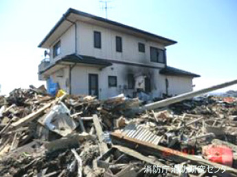 建物の焼損状況（県道10号沿いの作業場と燃焼した車両の影響で外壁の焦げた住宅）（2）